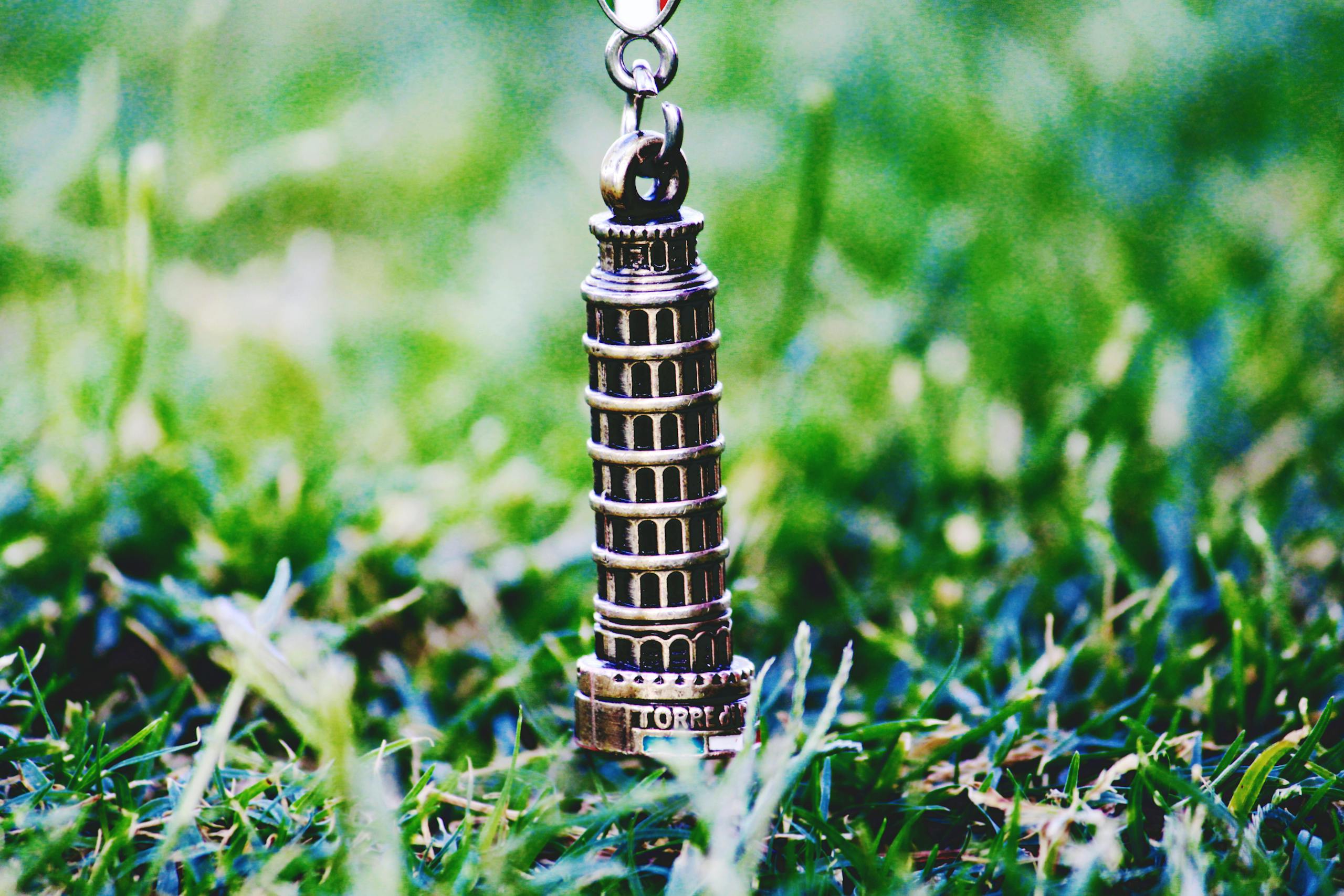 Keychain of Leaning Tower of Pisa in a grassy field. Perfect for travel and souvenir themes.